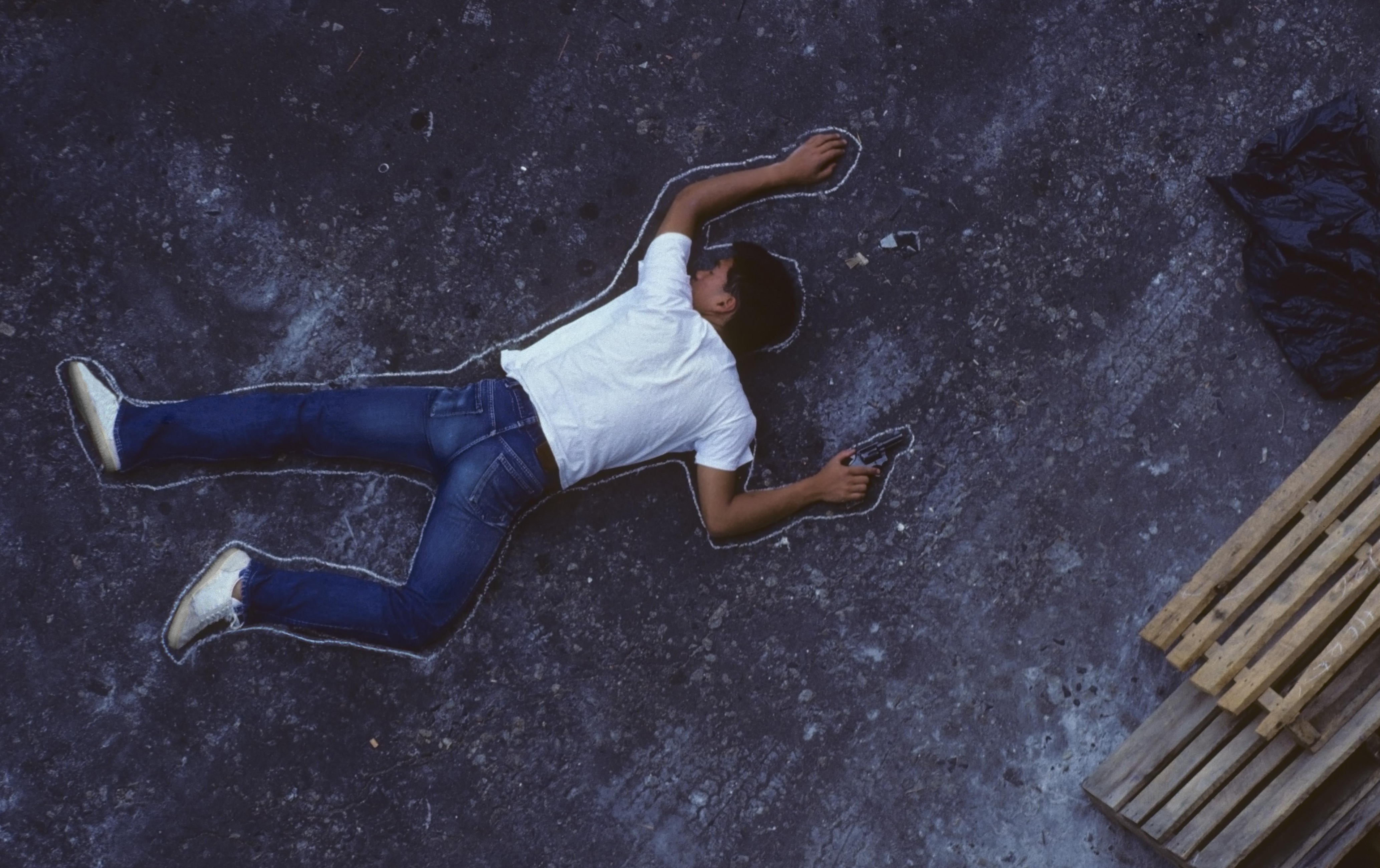 Man with gun lying on ground, chalk outline around him, elevated view