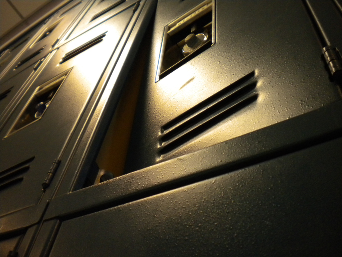 Close-up view of a damaged and jammed metallic blue locker illuminated by warm lighting with blurry background of other lockers and ceiling
