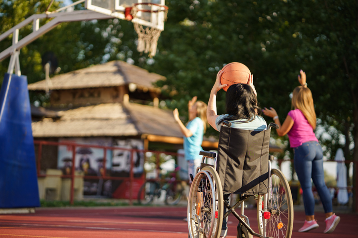 Woman in a wheelchair holds a ball while playing basketball with her friends