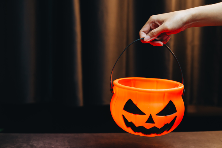 Halloween concept. Hand Holding Halloween Pumpkin Bucket with Spooky Face for Trick or Treat Activities and Festive Celebrations at Night